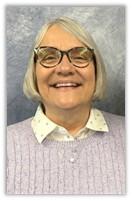 “Portrait of the Financial Secretary at Cheshire Lutheran Church, wearing glasses, a light purple sweater, and a white patterned collared shirt, smiling against a gray-blue textured backdrop